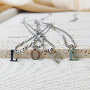 Detail of silver box chain necklaces featuring polished LOVE letter pendants on a stone display