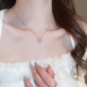 Close-up of a silver clover necklace with zircon inlay worn by a model on a white top