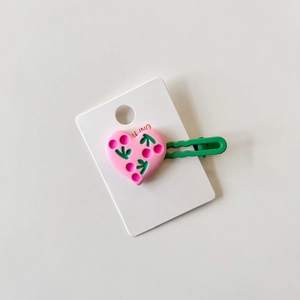 Detail of pink resin heart hair clip with green cherry pattern on white card