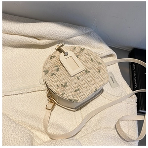 Detail of round straw crossbody bag with floral embroidery on white knitted background