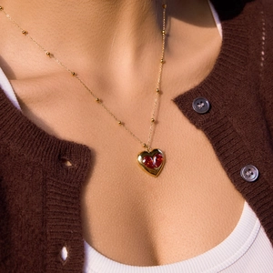 Collier élégant à chaîne dorée avec pendentif cœur rouge rubis porté par un mannequin
