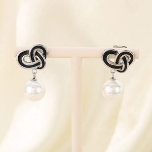 Detail of silver heart-knotted earrings with black enamel and hanging white pearl