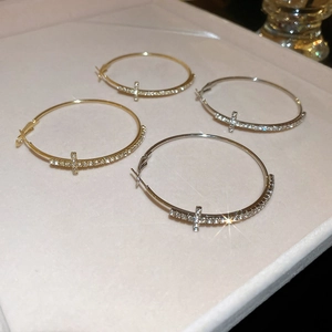Gros plan de créoles en or et argent avec détail de croix sertie de diamants