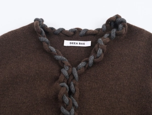 Détail du cardigan en tricot marron avec bordure tressée grise et étiquette au col