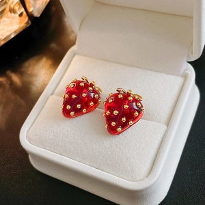 Macro shot of 3D red strawberry stud earrings with golden seeds in white jewelry box