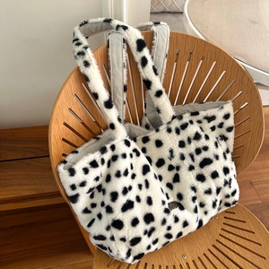 Fuzzy cow print plush tote bag with shoulder straps displayed on a wooden chair