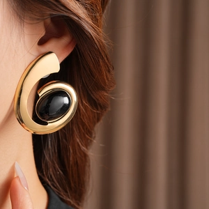 Close-up of a vintage gold swirl earring with a black oval stone on a female model