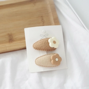 Detail of two floral felt BB hair clips in milk tea tones on white fabric display