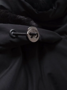 Detail der verstellbaren Metallkordel und Kunstpelzbesatz an einer schwarzen Windjacke