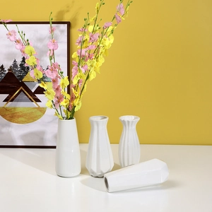 Set of four minimalist white ceramic vases with colorful artificial flowers on a plain surface