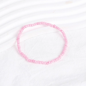 Detail of a handmade pink seed bead bracelet on a textured white fabric background