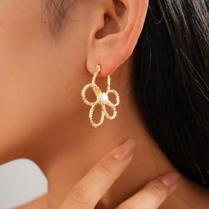 Detailansicht eines goldenen hohlen Blumenohrrings mit Perlenmitte an einem Modell