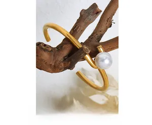 Detailed close-up of a minimalist gold-plated bangle with a large pearl on a wooden branch