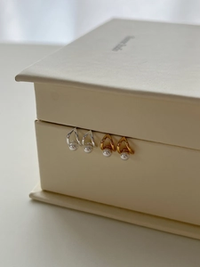 Detail view of 925 silver and gold triangle pearl earrings on a cream leather box