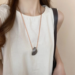 Detailed view of a vintage silver shell pendant on a thin brown cord worn by a model