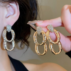 Close-up of golden oval double-hoop earrings with textured metal and shimmering zircons