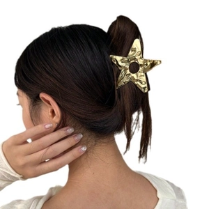 Golden hollow star hair claw clip with wrinkled metal texture worn by a model