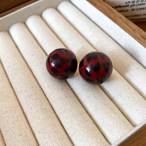 Close-up of red leopard print resin ball earrings set in a beige velvet jewelry box