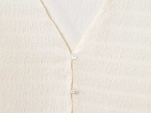 Dettaglio del tessuto crepe a bolle bianco crema con scollo a V e bottoni bianchi