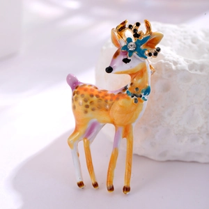 Détail d'une broche cerf peinte avec bordure dorée et strass sur fond doux