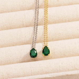 Detail of silver and gold necklaces with green teardrop emerald pendants on a beige mat