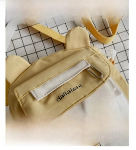 Detail presentation of yellow canvas shoulder bag with bear ear design and badges
