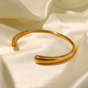 Polished 18K gold stainless steel cuff bracelet on elegant beige silk fabric texture