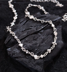 Detail view of silver metal bracelet with heart and clover charms on dark stone texture