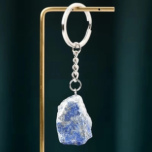 Natural raw blue lapis lazuli stone keychain on gold display stand with textured background