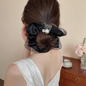 Detail of a black satin organza scrunchie with pearls and rhinestones on a bun hairstyle