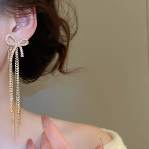 Macro shot of elegant gold bow tassel earrings with sparkling zircons on female model
