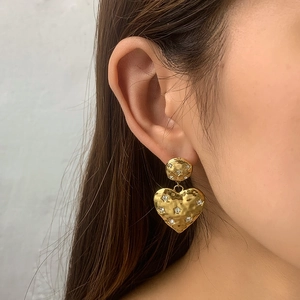 Close-up of heart-shaped gold earring with hammered texture and star-set cubic zirconia