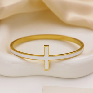Dettaglio del bracciale in acciaio dorato con croce in smalto bianco su vassoio in ceramica