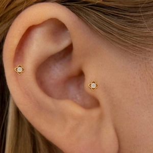 Close-up of sparkling gold clover stud earrings with pavé diamonds on model's ear