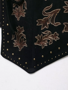 Detailed macro view of black suede vest with brown floral embroidery and gold metal studs
