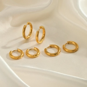 Three pairs of varied size minimalist golden stainless steel hoop earrings on silk