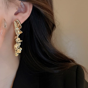 Close-up of golden irregular lava-textured long earrings on model with metallic finish