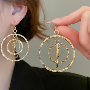 Close-up of golden geometric hollow hoop earrings with textured layered circular design