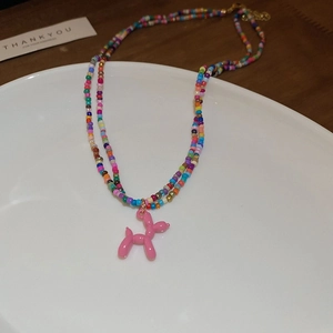 Rainbow beaded necklace with pink balloon dog pendant on white ceramic plate