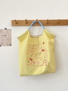 Detail of yellow canvas tote bag with cherry embroidery and blue striped handles