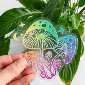 Close-up of rainbow prism mushroom and moon suncatcher sticker against green leaves
