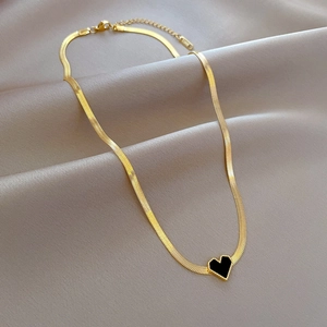 Detail of a gold snake chain necklace with a black heart pendant on champagne silk fabric