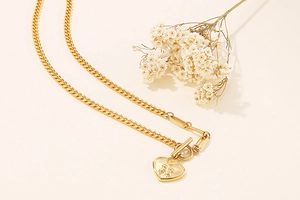 Detail of gold titanium heart pendant with embossed figures on Cuban and paperclip chain