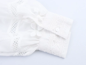 Dettaglio della manica di una camicia bianca in cotone con pizzo e ricami floreali