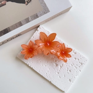 Detail of orange resin flower hair claw clip with translucent daisy petals and red beads