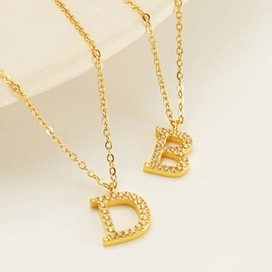 Close-up of gold titanium steel necklaces with diamond-encrusted B and D letter pendants