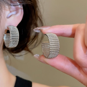 Macro detail of silver C-shaped hoop earrings featuring a modern mesh weave texture
