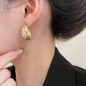 Close-up of a model wearing twisted golden earrings with a unique hammered texture finish
