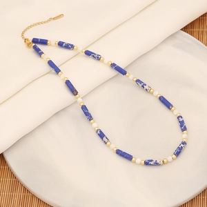 Dettaglio collana di perle con pietre blu e perline dorate su vassoio di marmo
