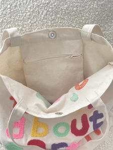 Detail view of canvas tote featuring colorful letter embroidery and magnetic snap closure